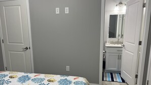 A bedroom with a bed, a door, a bathroom with a sink and mirror, and a hallway.