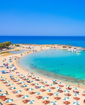A beach with numerous umbrellas and sun loungers, a clear blue sea, and boats in the water. - Phaedra - Vacation house with private pool in Kounoupidiana, Crete (Vamvakópoulo)
