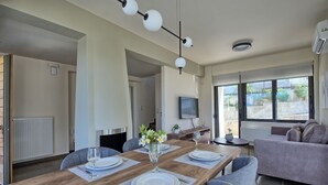 Un espace repas moderne avec une table en bois dressée pour quatre personnes, un canapé gris et un téléviseur fixé au mur.
