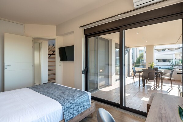 A modern hotel room with a bed, a TV mounted on the wall, a sliding glass door leading to a balcony with outdoor seating. - Phaedra - Vacation house with private pool in Kounoupidiana, Crete (Vamvakópoulo)