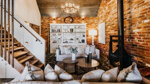 Una sala de estar acogedora con pared de ladrillo, chimenea blanca, una escalera y una estantería llena de libros y objetos decorativos.