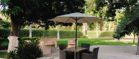 Un patio al aire libre con una mesa y sillas, rodeado de abundante follaje y árboles.