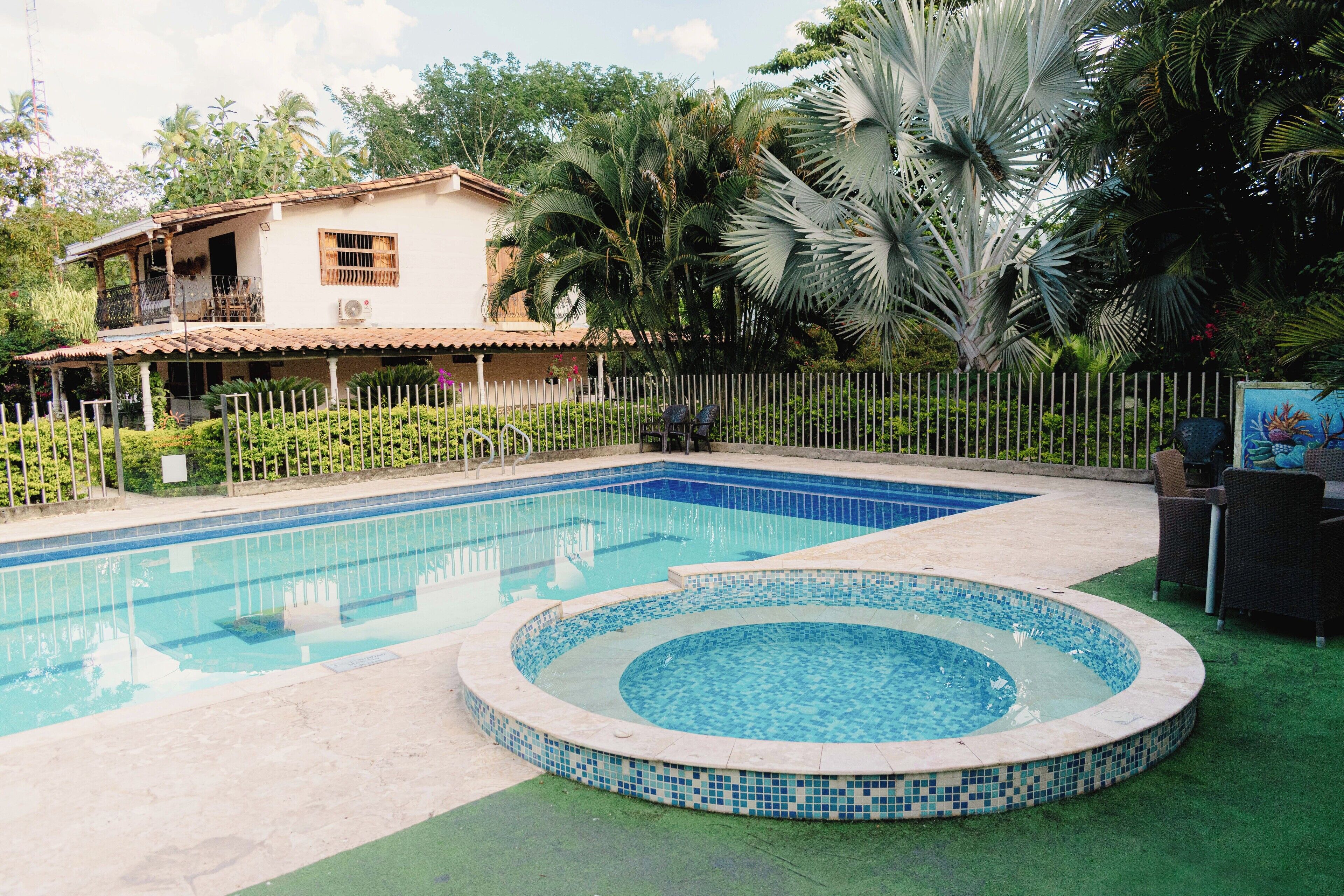 Una piscina con hidromasaje, rodeada por una cerca y vegetación.