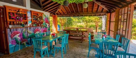 Un patio al aire libre con mesas y sillas de madera, rodeado por un techo y paredes de madera rústica.
