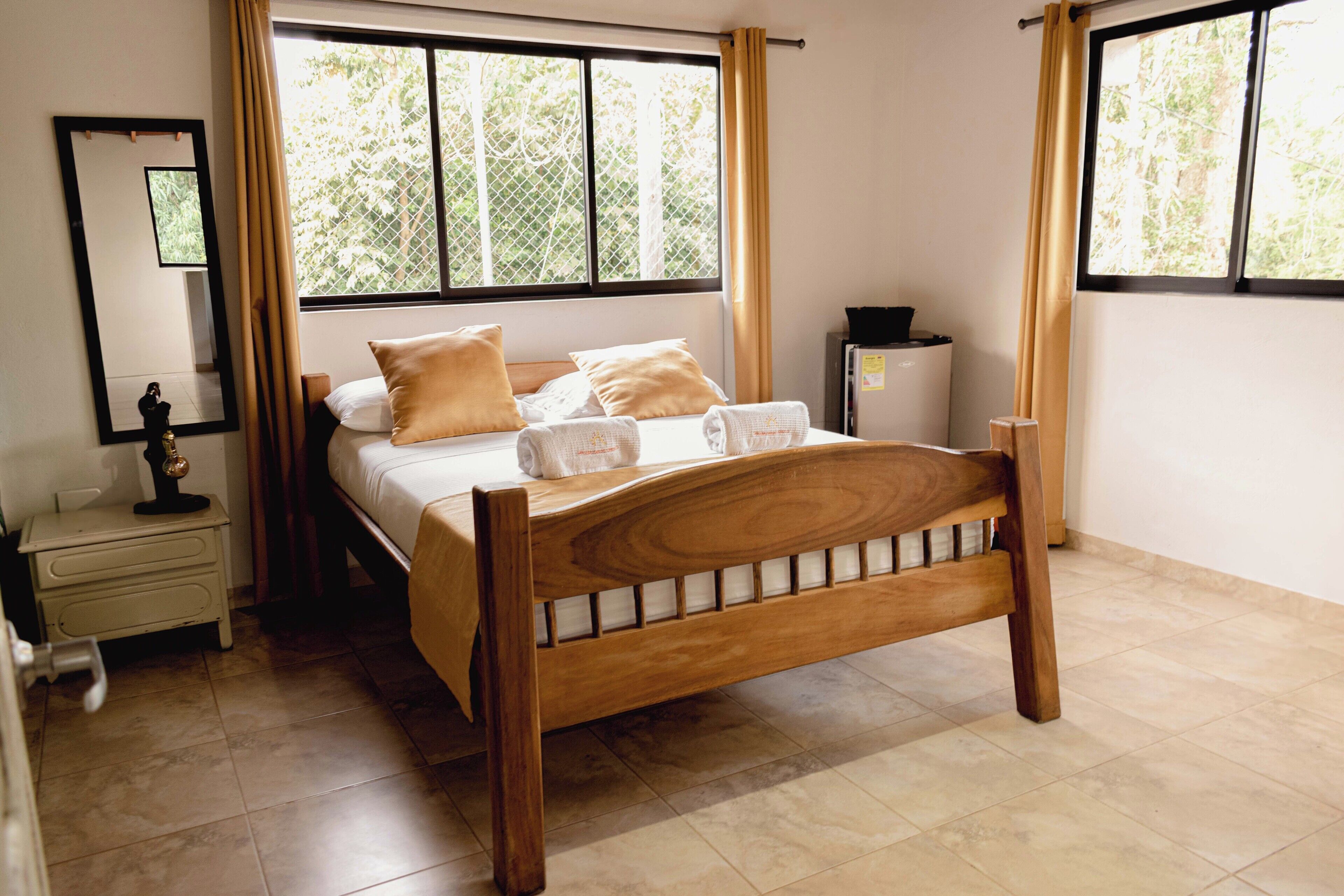 A bedroom with a wooden bed, a nightstand, a mirror, and a window with curtains.