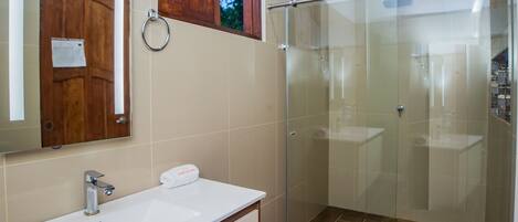 A modern bathroom with a wooden ceiling, a glass shower enclosure, a white sink, and a mirror.