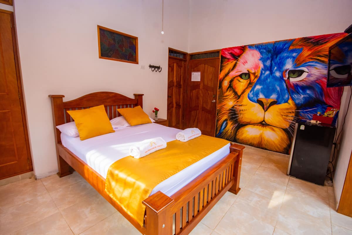 Un dormitorio con una cama de madera, un cuadro grande de un león y un refrigerador pequeño.