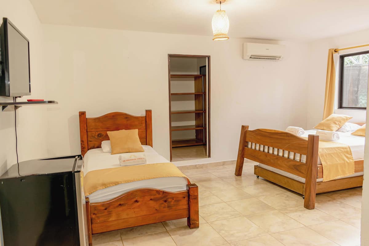 Un dormitorio con dos camas de madera, un televisor, un armario y un equipo de aire acondicionado.