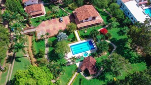 Vue aérienne d’un quartier résidentiel avec une piscine, plusieurs maisons et une végétation luxuriante.