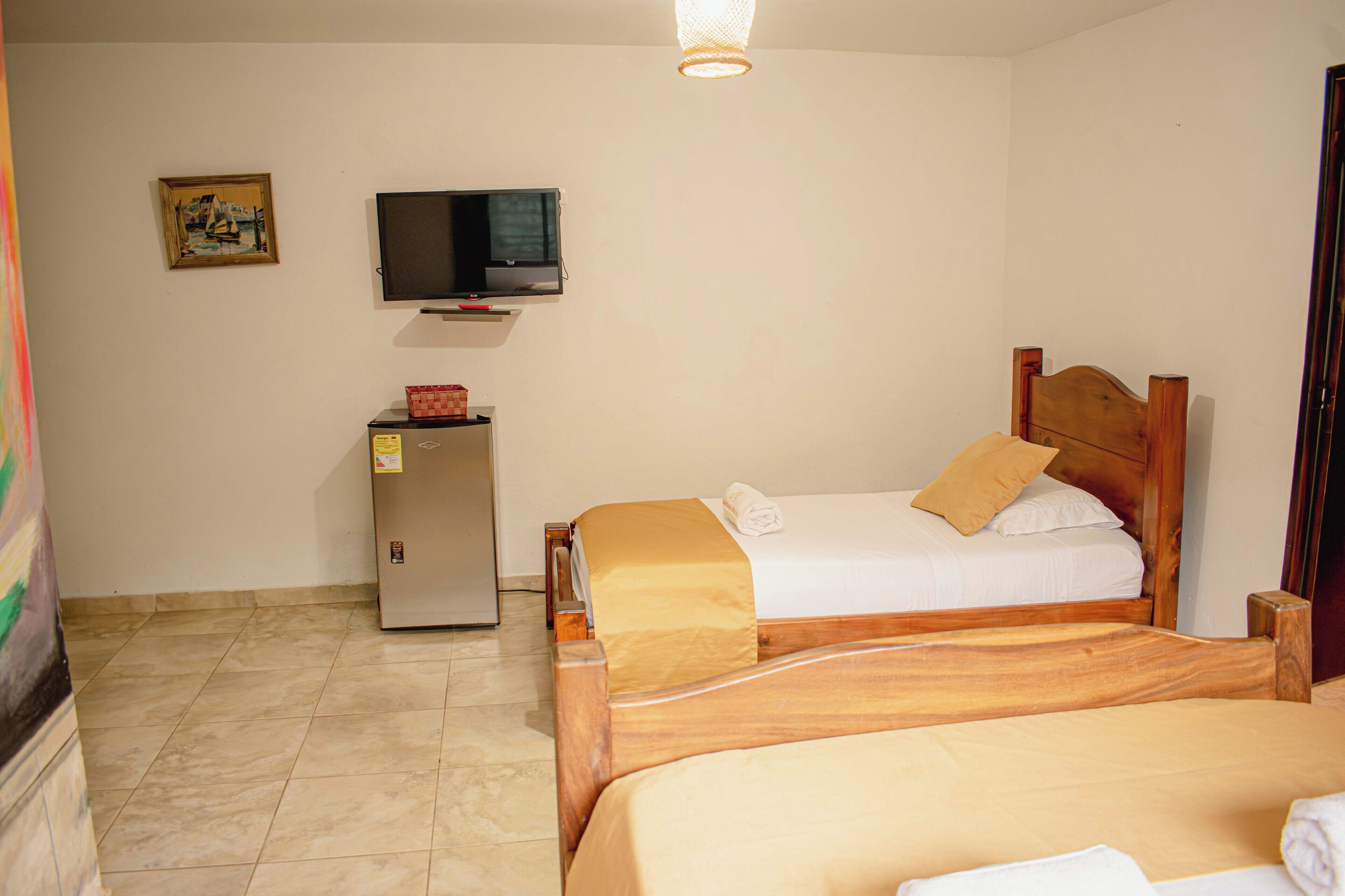 A hotel room with a double bed, a television mounted on the wall, a small desk with a computer, and a refrigerator.