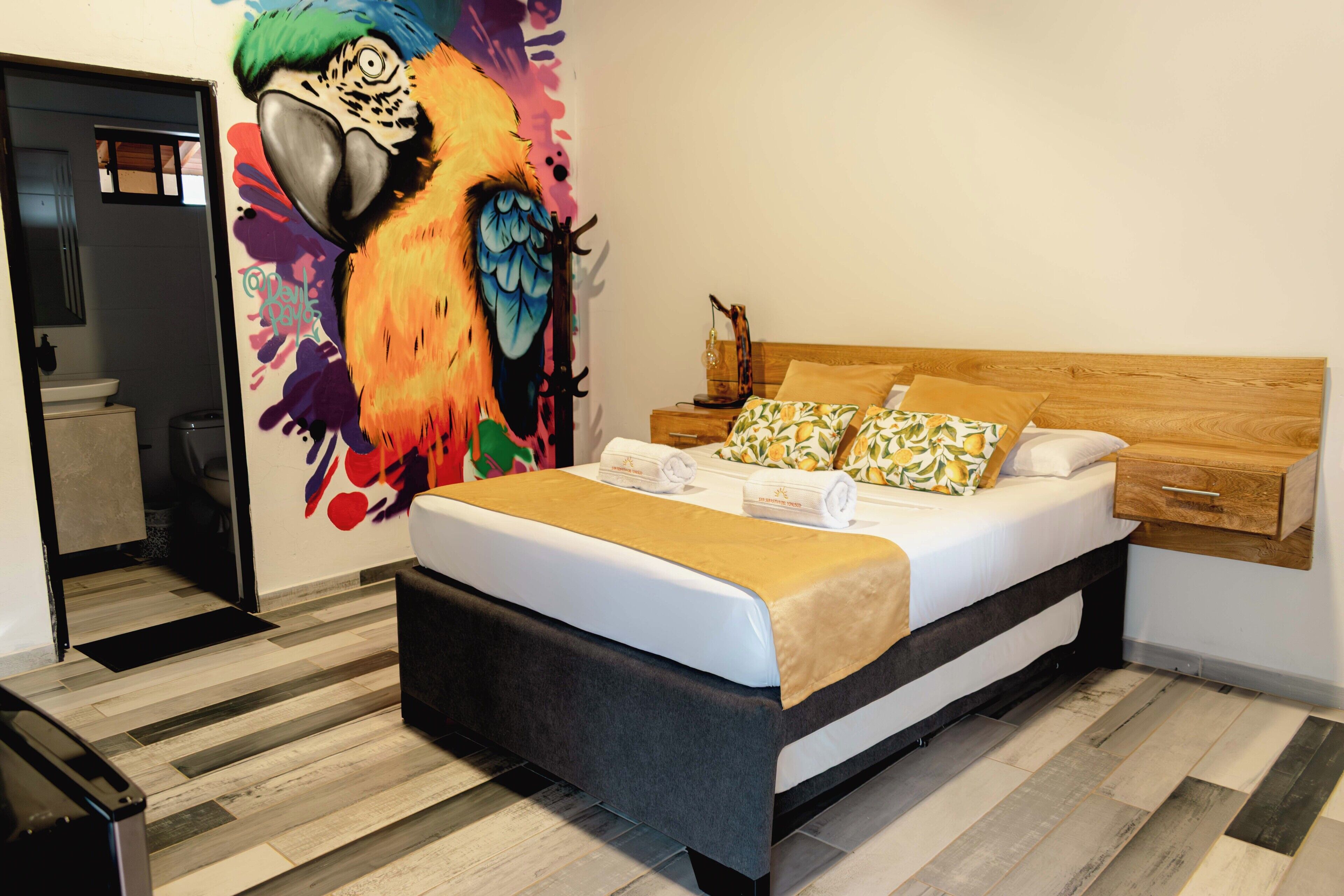 Un dormitorio con cama, cabecera de madera, mesita de noche, pintura en la pared y suelo de madera.