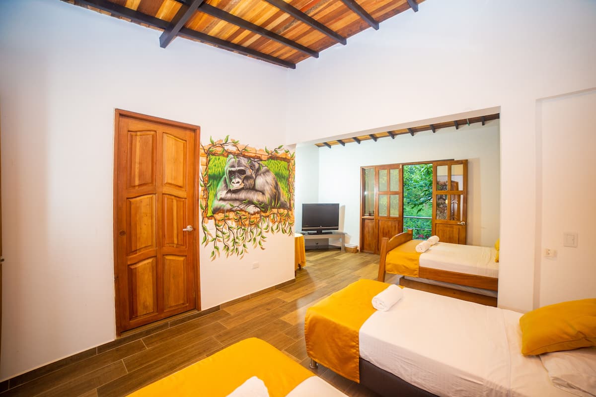 Habitación con dos camas, televisor y un mural de un gorila.