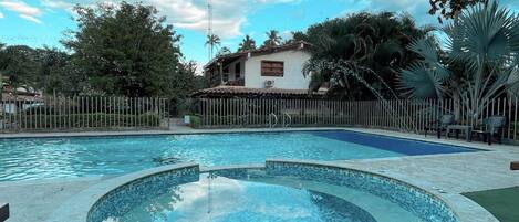 A swimming pool with a circular hot tub area, surrounded by a fence and palm trees.