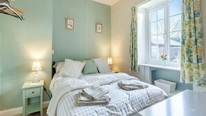 A neatly arranged bedroom with a bed, bedside lamps, a nightstand, a window with curtains, and a small table by the window. - 3 bedroom accommodation in Colyton, near Lyme Regis (Colyton, near Lyme Regis)