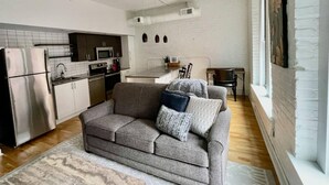 A compact living space with a kitchenette, a grey sofa with patterned cushions, and a patterned rug. - This serviced apartment is a 4 bedroom(s), 4 bathrooms, located in Omaha, NE. (Omaha)