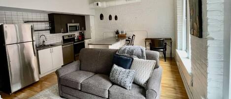 A compact living space with a kitchenette, a grey sofa with patterned cushions, and a patterned rug.