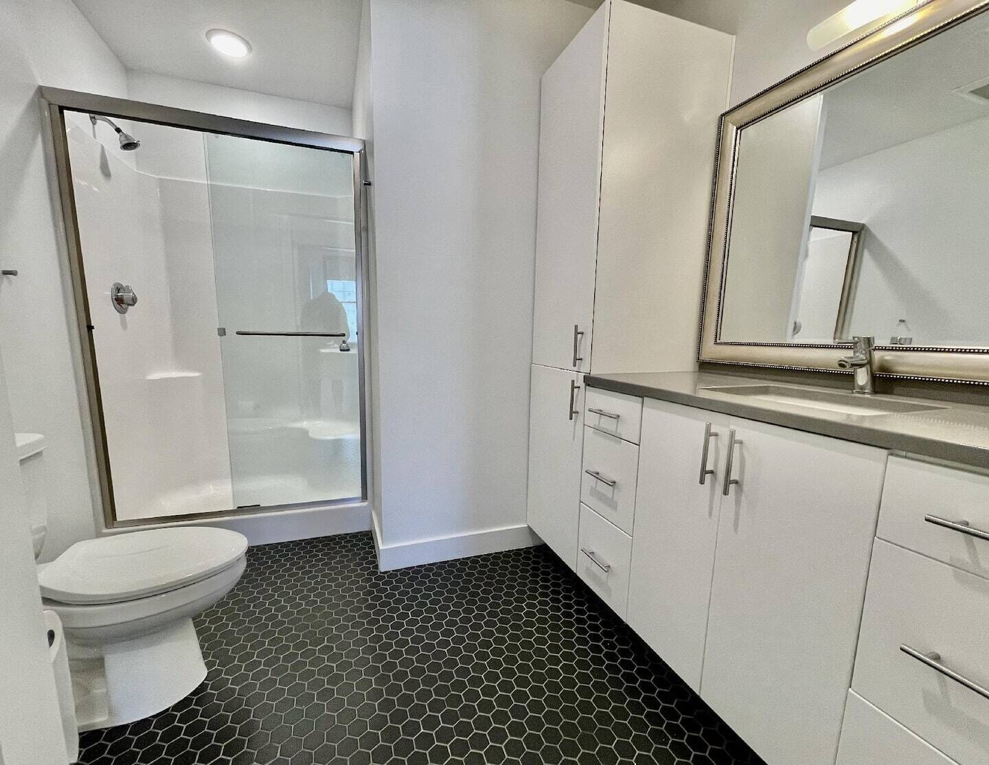 Une salle de bain moderne avec une douche à parois de verre, des toilettes et des meubles blancs.