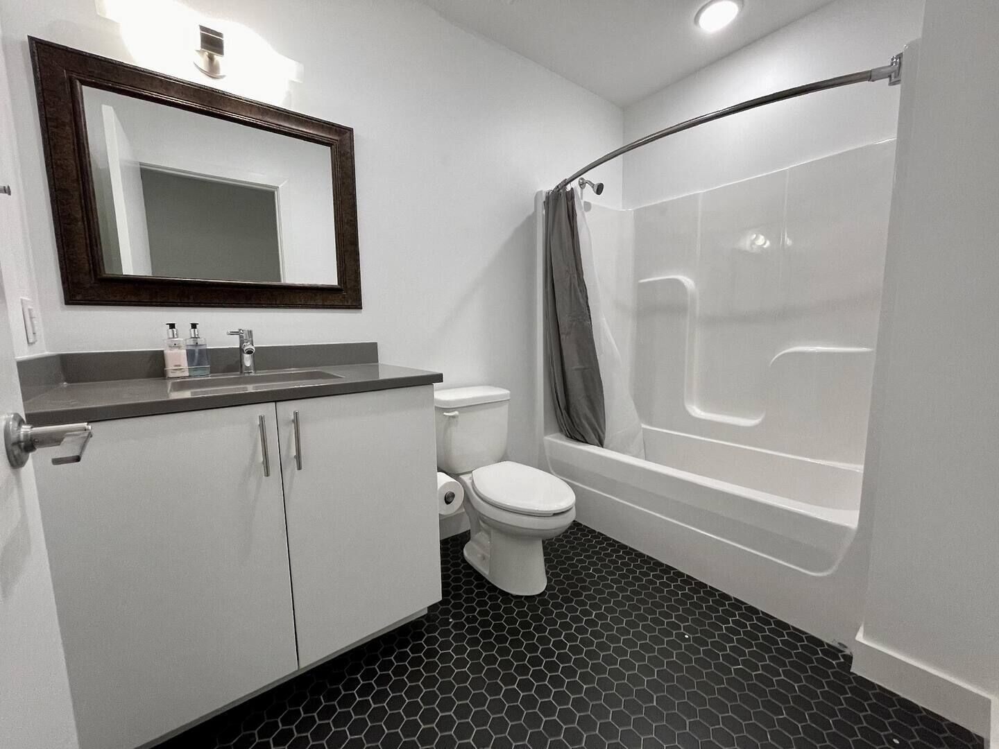 A bathroom with a toilet, sink, mirror, and a shower with a curved tub.