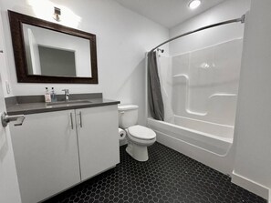 A bathroom with a toilet, sink, mirror, and a shower with a curved tub.