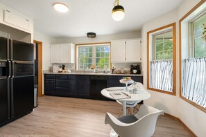 A modern kitchen with white cabinets, a black refrigerator, and a dining area with a white table and chair.