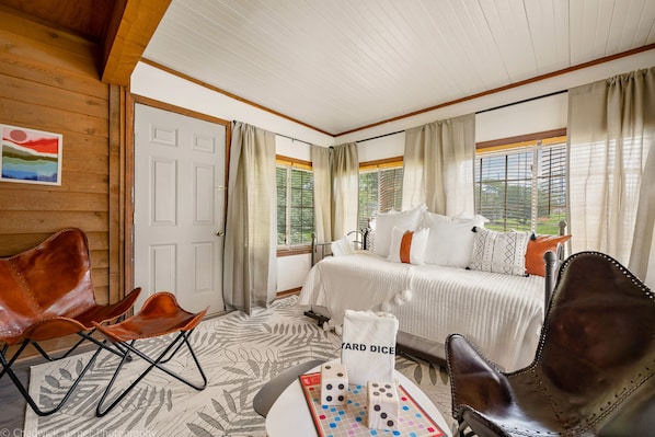 A hotel room with a bed, two leather chairs, a table with dice and a towel, and a painting on the wall.