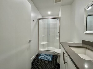 Un baño moderno con cabina de ducha de vidrio, inodoro y lavamanos.