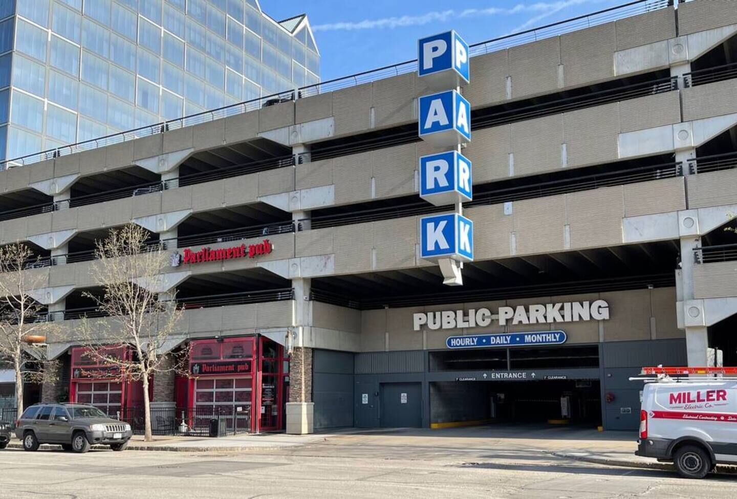 Een meerlaagse openbare parkeergarage met duidelijke borden waarop 'PARKING' en 'OPENBAAR PARKEREN' staan, met vermelding van uurtarieven, dagtarieven en maandelijks tarieven.