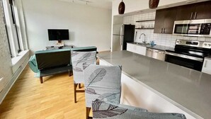 Eine moderne Küche mit einer zentralen Kochinsel, Edelstahlgeräten und einem Essbereich mit Fernseher und gemusterten Stühlen.