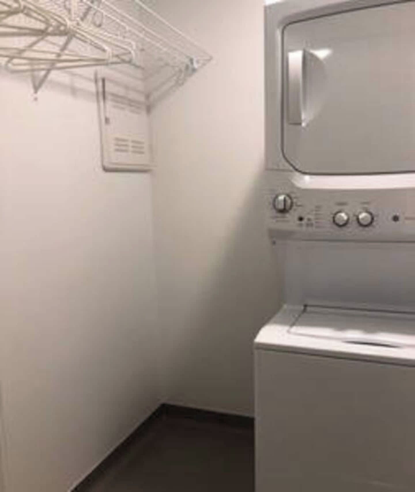 Uma lavanderia com máquina de lavar e secadora empilhadas, um varal e um painel de controle.