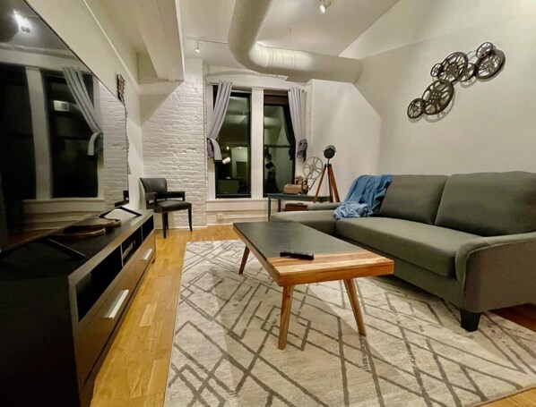 Ein modernes Wohnzimmer mit grauem Sofa, einem Holztisch, einem Fernseher und einem gemusterten Teppich.