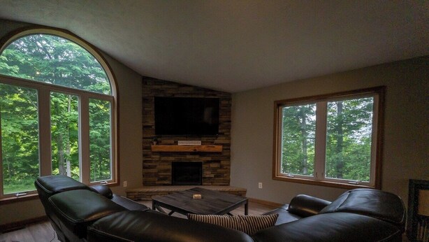 A living room with a stone fireplace, leather sofas, and large windows with a forest view.
