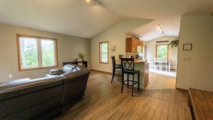 A spacious living area with a dark leather sofa, wooden flooring, and a kitchen area with a dining table and chairs.