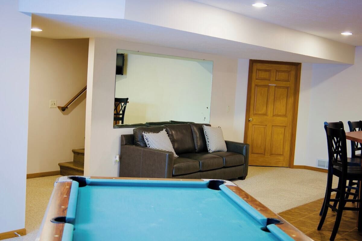 A living room with a pool table, a brown leather sofa, a wooden door, and a staircase leading to another room.