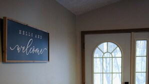 A hallway with a wooden bench, a welcome sign, and a door with a window.