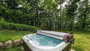 A hot tub in a lush garden with a wooden deck and a bench.