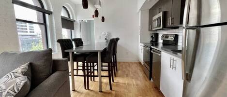 A modern kitchen with stainless steel appliances, a dining area with a table and chairs, and a sofa with patterned cushions.