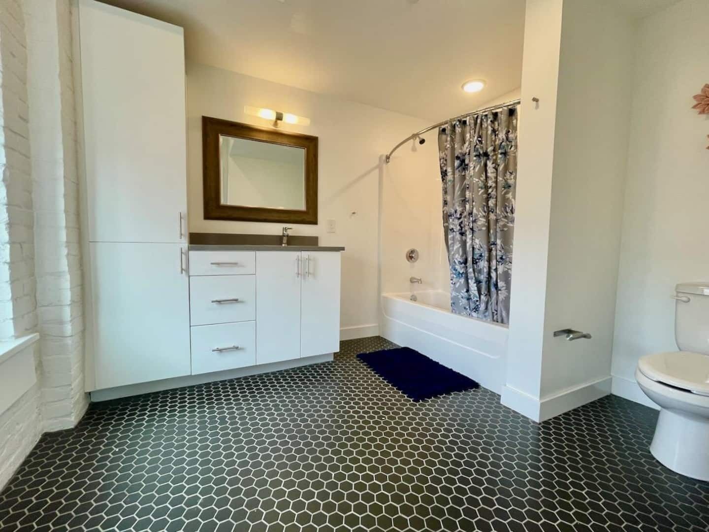 A bathroom with a white vanity, a mirror, a shower with a floral curtain, and a toilet.