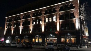En byggnad med flera våningar, en fasad av tegel och upplysta fönster, samt en restaurang på markplan med uteservering.