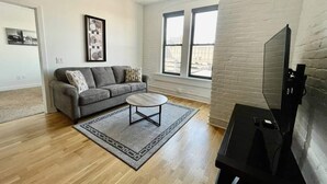 Ein modernes Wohnzimmer mit grauem Sofa, einem Couchtisch und einem Flachbildfernseher.
