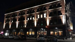 Ein mehrstöckiges Gebäude mit Backsteinfassade und beleuchteten Fenstern, mit einem Restaurant im Erdgeschoss und Außenbereich.