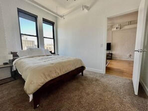 Une chambre avec un grand lit, deux fenêtres et une vue sur la ville.