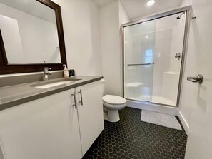 Une salle de bain équipée d’un lavabo, d’un miroir, de toilettes et d’une douche à parois de verre.