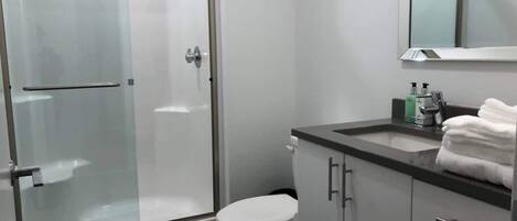 A modern bathroom with a glass shower enclosure, a toilet, a sink with a mirror above, and a towel rack.