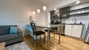 Een ruimtelijke zithoek met een kitchenette, een eettafel, een bank en een tapijt met een patroon.