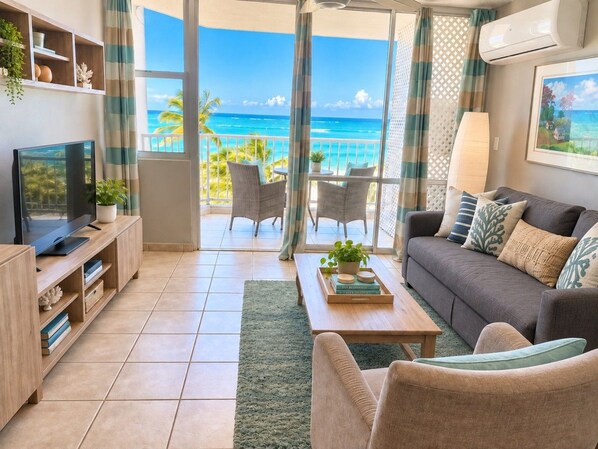 A living room with a television, sofa, coffee table, and a view of the ocean.