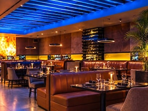 Ein Restaurant mit Ledersitzbänken, gedeckten Tischen und Weingläsern sowie einer Bar mit Flaschenregalen.