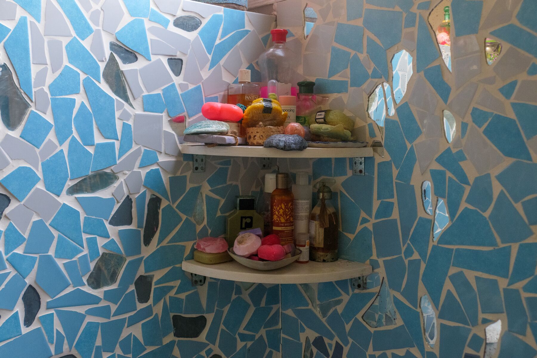 Une salle de bain avec un mur recouvert de mosaïques et des étagères où sont rangés les articles de toilette.