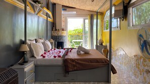 Une chambre à coucher avec un lit, des tables de chevet, une lampe, une cheminée et une vue sur l’extérieur.
