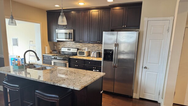 A modern kitchen with dark cabinetry, stainless steel appliances, a granite countertop, and a large island with bar stools. - Charming 4 Br 2Ba Duplex  (Baltimore)