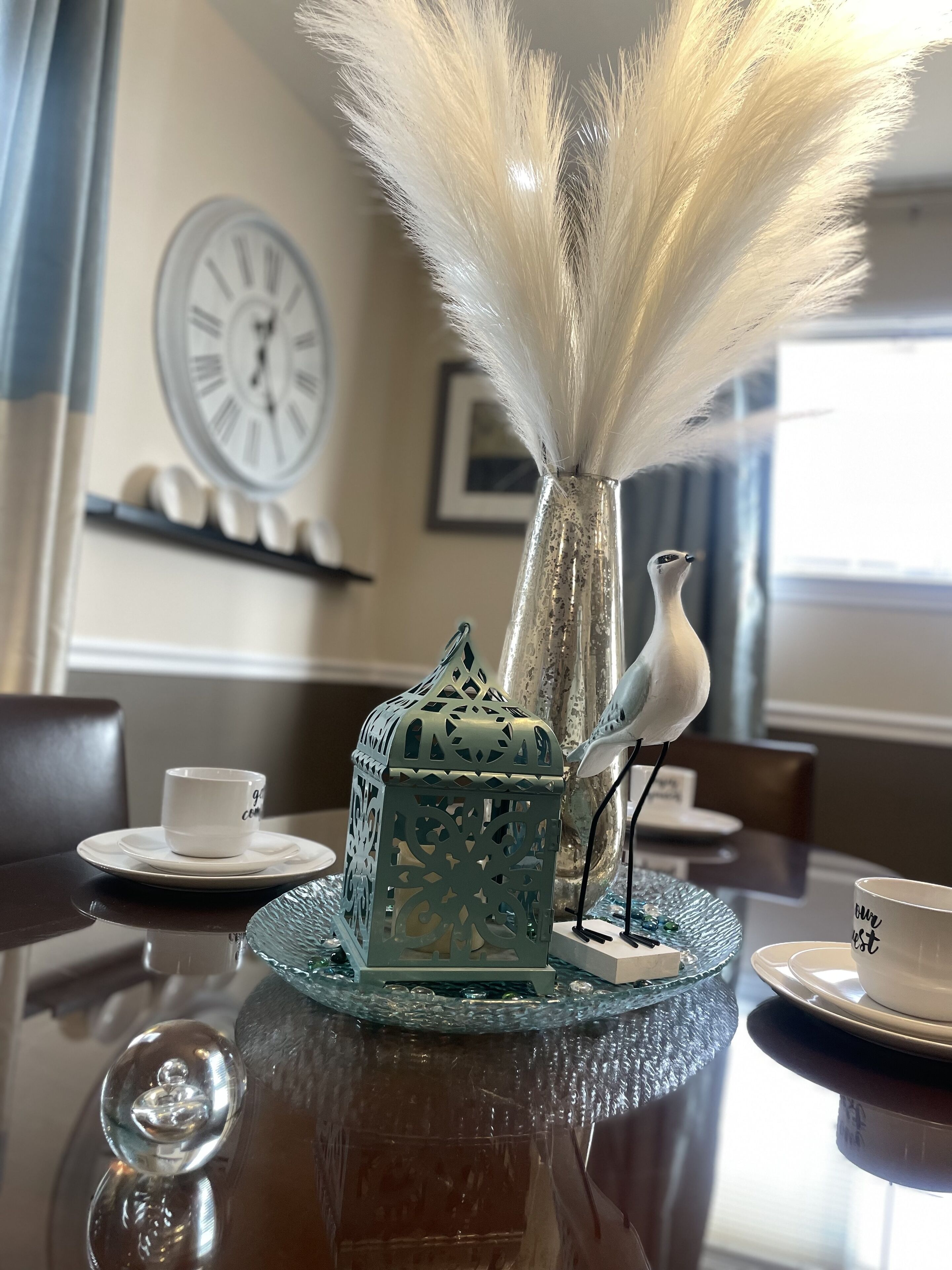 A table with a decorative glass centerpiece featuring a bird figurine and a vase with white feathers.